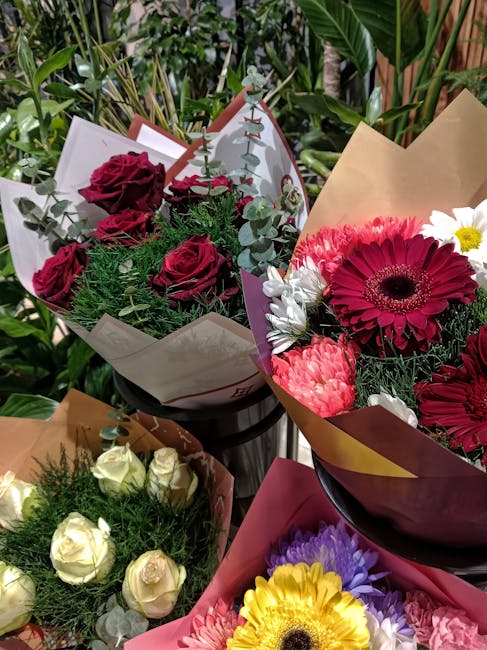 A vibrant display of fresh flower bouquets arranged on a surface, featuring a variety of floral arrangements with rich colors and textures. One bouquet contains deep red roses intertwined with green f