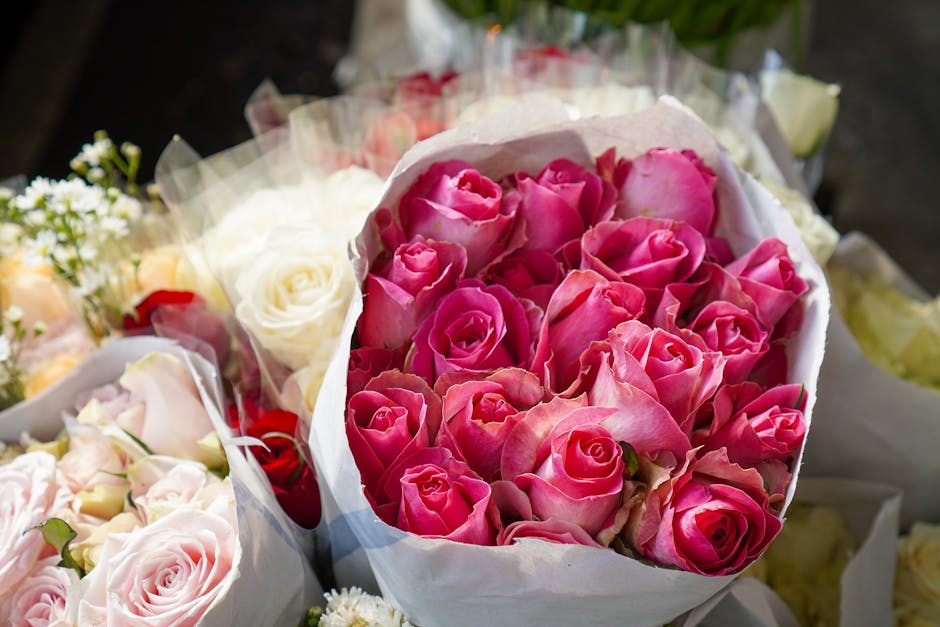 A bouquet of fresh pink roses with tightly closed buds and velvety petals, wrapped in white tissue paper. The bouquet is arranged with a mix of fully bloomed roses and partially opened buds, showcasin