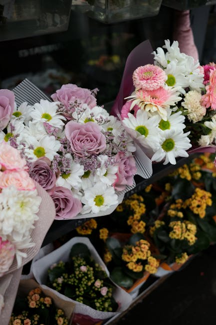 A vibrant display of fresh floral bouquets arranged with pink roses, white daisies with yellow centers, and delicate pink gypsophila, wrapped in light pink and purple paper with subtle paper textures.