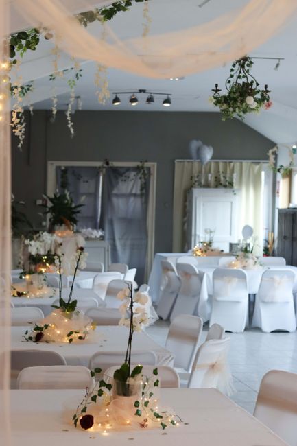 Elegant wedding reception setup featuring tables decorated with floral arrangements and ambient fairy lights. The tables are covered with white tablecloths and adorned with small bouquet centerpieces 